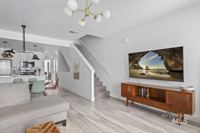 living room with a textured ceiling, light hardwood / wood-style floors, an inviting chandelier, and sink