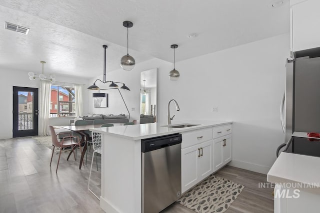 kitchen featuring kitchen peninsula, appliances with stainless steel finishes, sink, pendant lighting, and white cabinetry