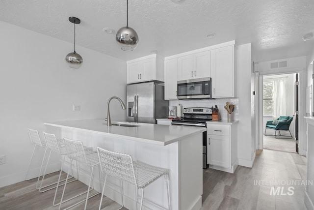 kitchen featuring appliances with stainless steel finishes, white cabinetry, pendant lighting, and sink