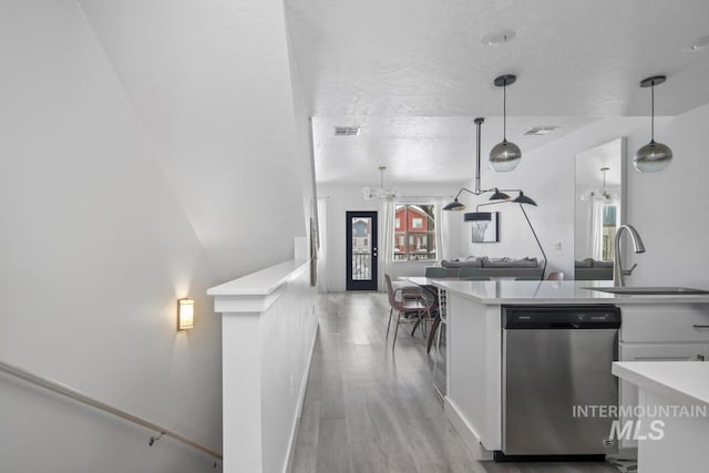 kitchen featuring sink, hanging light fixtures, stainless steel dishwasher, light wood-type flooring, and white cabinetry