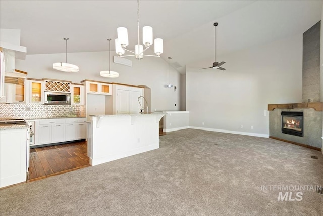 2249 N Eagle Creek Ln, Eagle, ID 83616 - kitchen with stainless steel microwave, high vaulted ceiling, a ceiling fan, a glass covered fireplace, and dark carpet