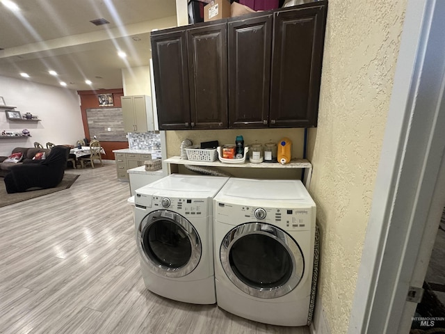 clothes washing area featuring light hardwood / wood-style floors, cabinets, and washing machine and clothes dryer