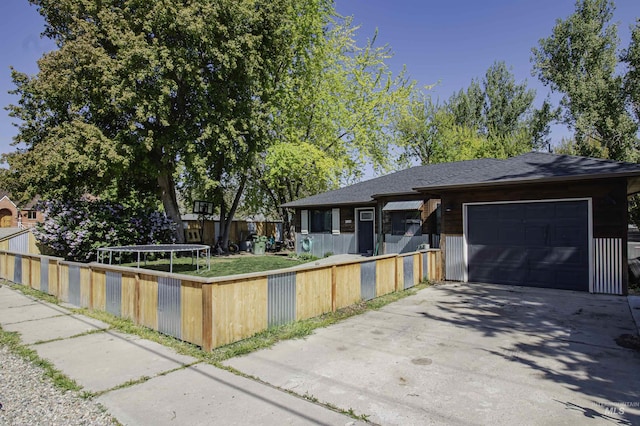 single story home with concrete driveway, an attached garage, a fenced front yard, and roof with shingles