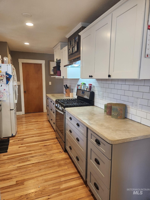 kitchen featuring stainless steel range with gas stovetop, light countertops, freestanding refrigerator, light wood-style floors, and under cabinet range hood