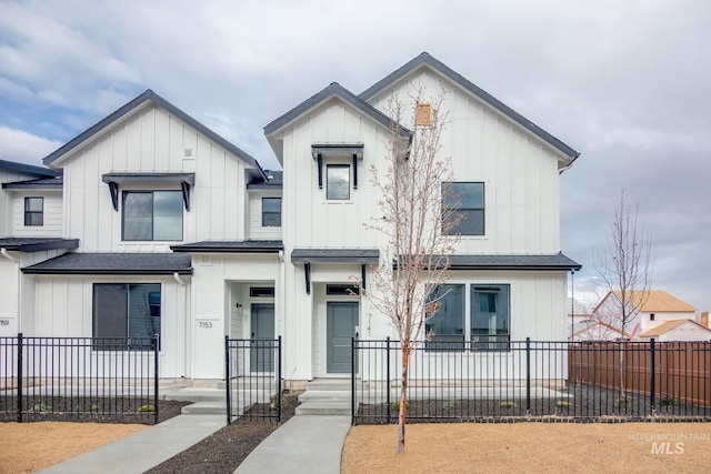 modern inspired farmhouse with a fenced front yard, board and batten siding, and roof with shingles