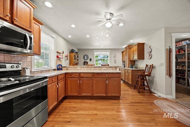 7425 Robinson Rd, Kuna, ID 83634 - kitchen featuring appliances with stainless steel finishes, a peninsula, light wood-style flooring, brown cabinetry, and a textured ceiling