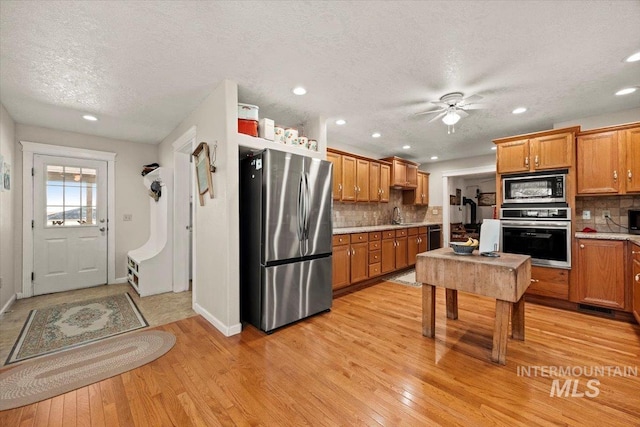 7425 Robinson Rd, Kuna, ID 83634 - kitchen featuring appliances with stainless steel finishes, light wood finished floors, a textured ceiling, decorative backsplash, and ceiling fan