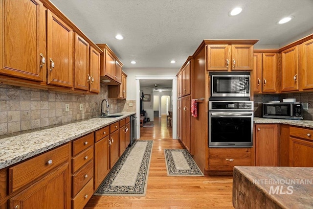 7425 Robinson Rd, Kuna, ID 83634 - kitchen featuring appliances with stainless steel finishes, brown cabinetry, light wood-type flooring, a ceiling fan, and decorative backsplash
