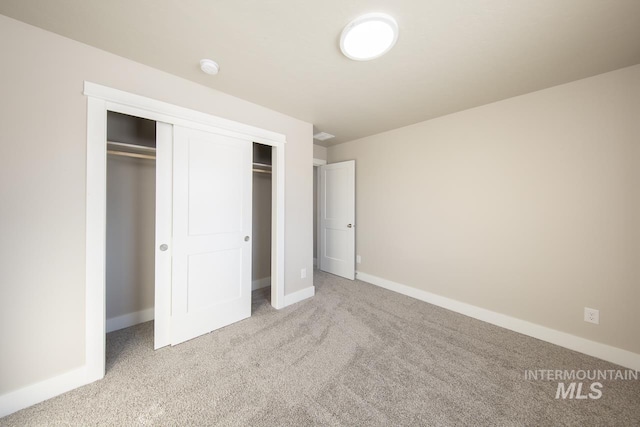 unfurnished bedroom featuring light carpet, a closet, and baseboards