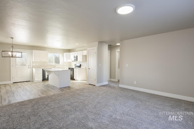 kitchen featuring a kitchen island, appliances with stainless steel finishes, open floor plan, light countertops, and white cabinetry