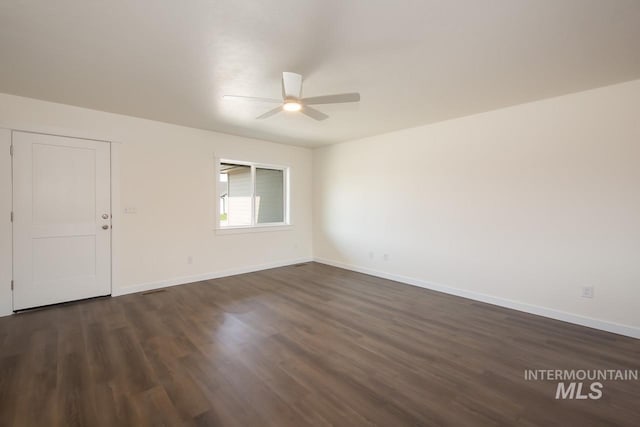 spare room featuring dark wood-style flooring, a ceiling fan, and baseboards