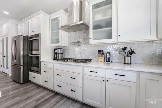 922 Victory Dr, Gooding, ID 83330 - kitchen featuring wood finished floors, appliances with stainless steel finishes, wall chimney exhaust hood, and white cabinetry
