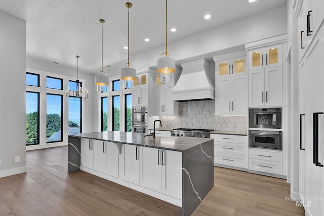 kitchen with white cabinetry, custom exhaust hood, decorative light fixtures, and a kitchen island with sink