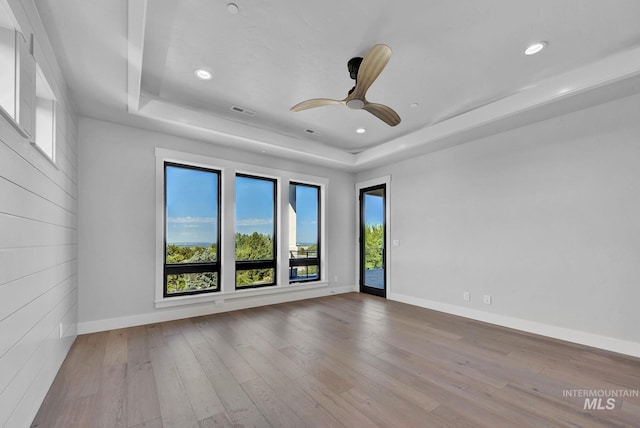 unfurnished room with ceiling fan, a tray ceiling, and light hardwood / wood-style floors