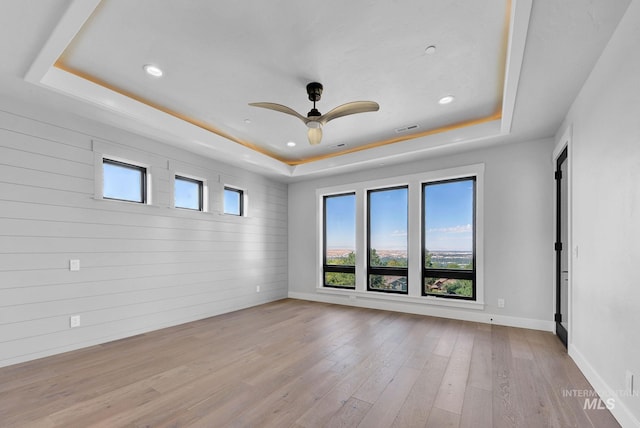 unfurnished room with ceiling fan, light hardwood / wood-style floors, and a tray ceiling