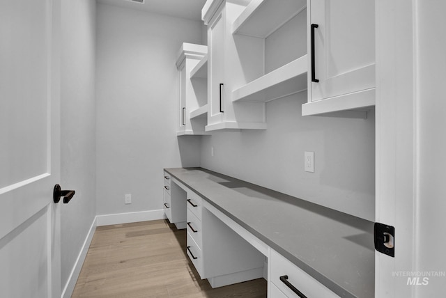 home office with built in desk and light hardwood / wood-style flooring