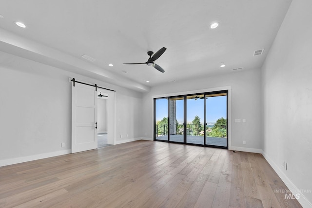 empty room with ceiling fan, a barn door, and light hardwood / wood-style flooring