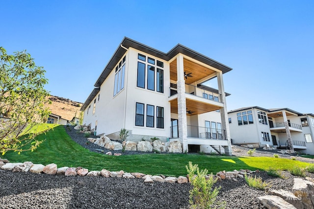 back of property featuring ceiling fan, a balcony, and a yard