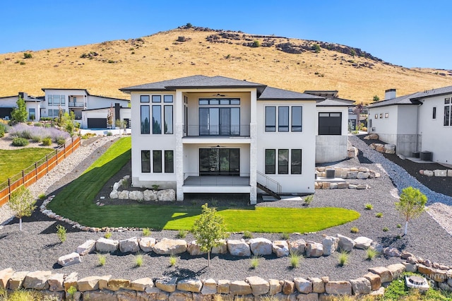 back of property with a mountain view, central air condition unit, a balcony, and a yard