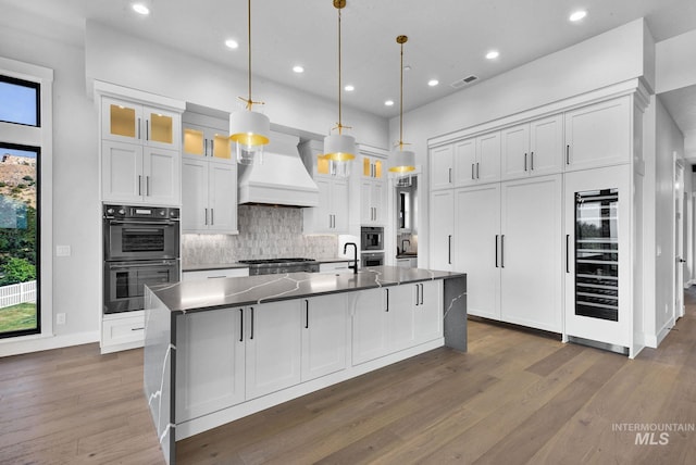 kitchen featuring premium range hood, double oven, white cabinets, and hanging light fixtures