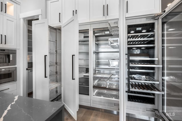 interior space with stainless steel oven, dark stone counters, dark hardwood / wood-style flooring, and white cabinetry