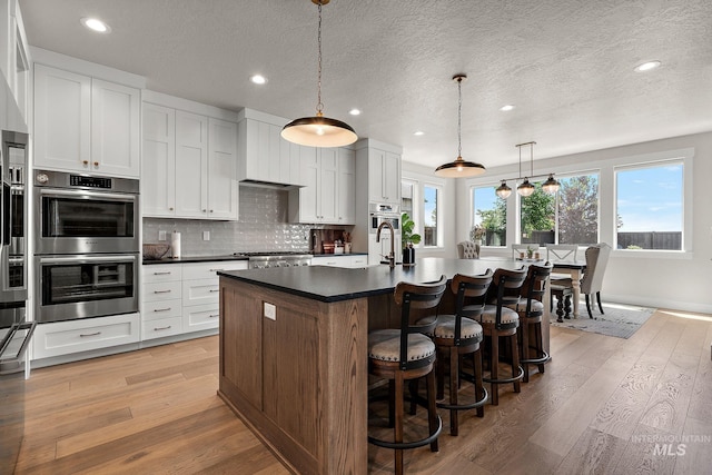 5209 W Strant Steet, Eagle, ID 83616 - kitchen featuring stainless steel double oven, dark countertops, a center island with sink, recessed lighting, and light wood-type flooring