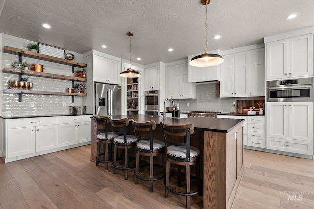 5209 W Strant Steet, Eagle, ID 83616 - kitchen featuring stainless steel appliances, dark countertops, light wood-type flooring, open shelves, and tasteful backsplash