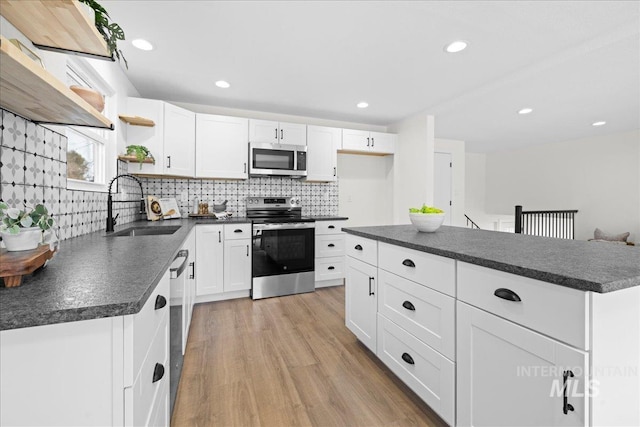 kitchen with stainless steel appliances, sink, white cabinetry, light hardwood / wood-style floors, and a kitchen island