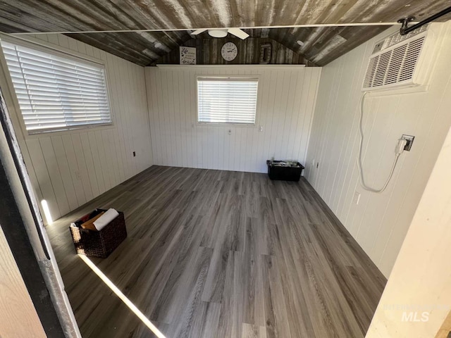 empty room featuring ceiling fan, lofted ceiling, wood walls, and wood finished floors