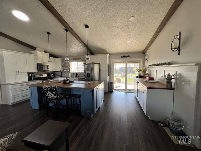 kitchen with butcher block counters, a textured ceiling, appliances with stainless steel finishes, and lofted ceiling with beams