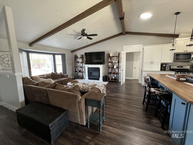 living area with a textured ceiling, dark wood-style flooring, vaulted ceiling with beams, baseboards, and ceiling fan