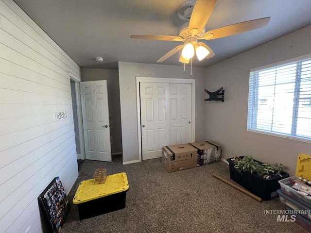 interior space with carpet, wood walls, and a ceiling fan