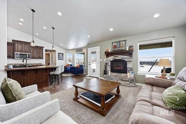 living area with a stone fireplace, a healthy amount of sunlight, wood finished floors, and vaulted ceiling