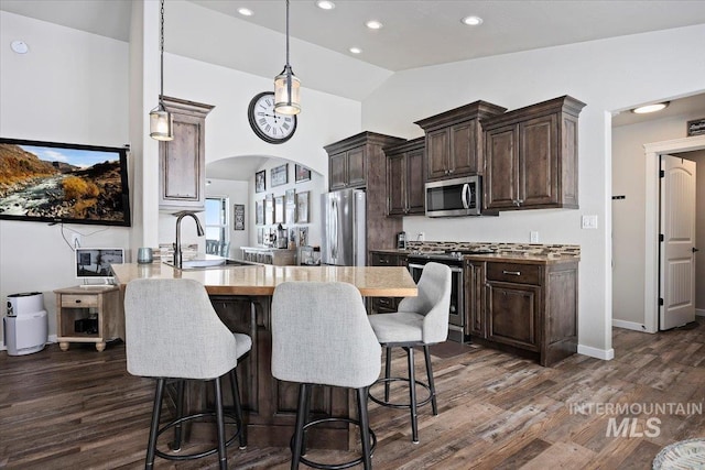 kitchen with a sink, a kitchen breakfast bar, dark wood finished floors, dark brown cabinetry, and appliances with stainless steel finishes