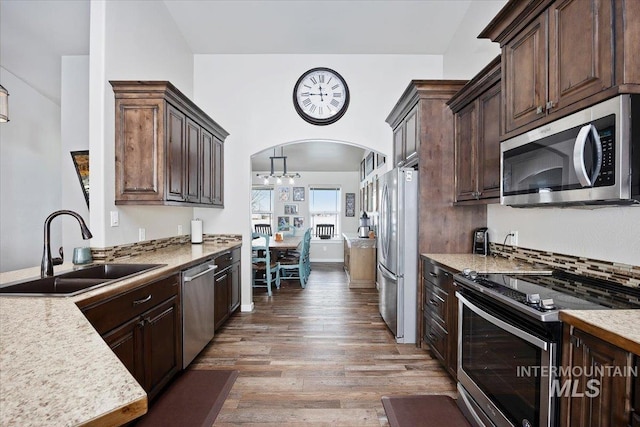 kitchen with dark brown cabinetry, appliances with stainless steel finishes, wood finished floors, arched walkways, and a sink