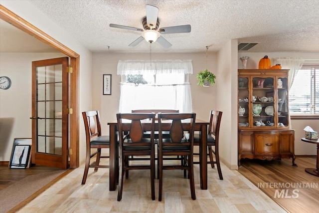 dining room with visible vents, baseboards, ceiling fan, light wood-type flooring, and a textured ceiling