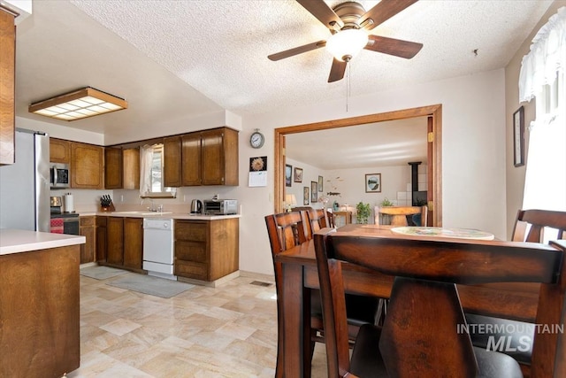 kitchen with a sink, stainless steel appliances, light countertops, a textured ceiling, and brown cabinets