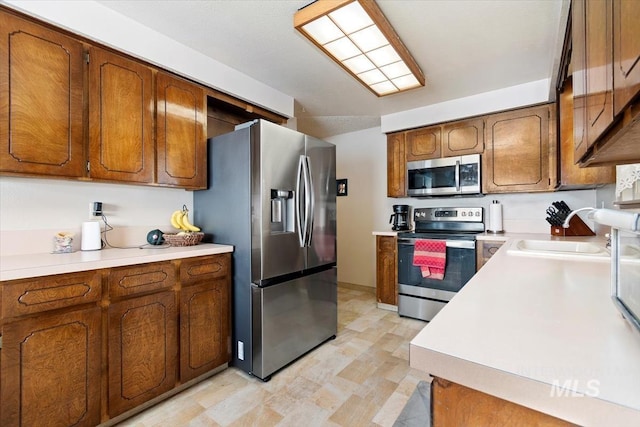 kitchen with light countertops, brown cabinetry, appliances with stainless steel finishes, and a sink