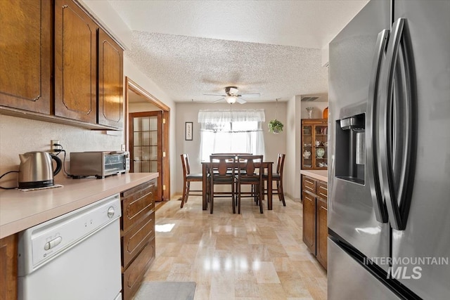 kitchen with a ceiling fan, a toaster, light countertops, dishwasher, and stainless steel fridge