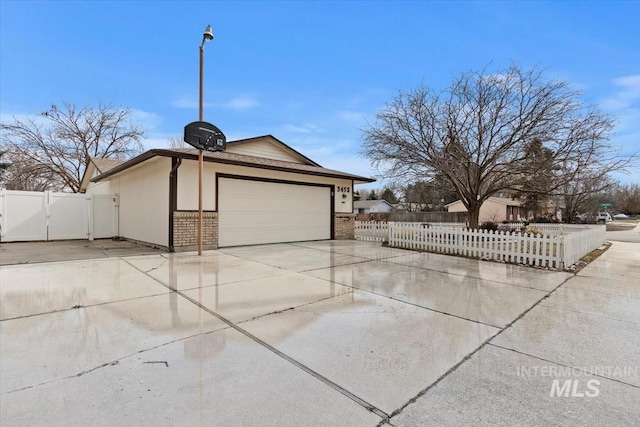 view of side of home featuring driveway, a gate, a fenced front yard, an attached garage, and brick siding