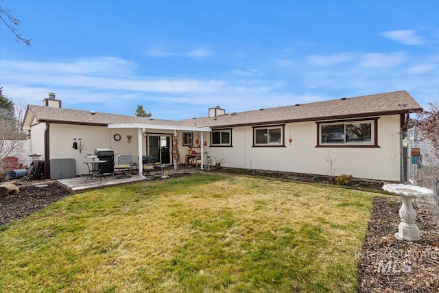 rear view of house with a patio, a lawn, and a chimney