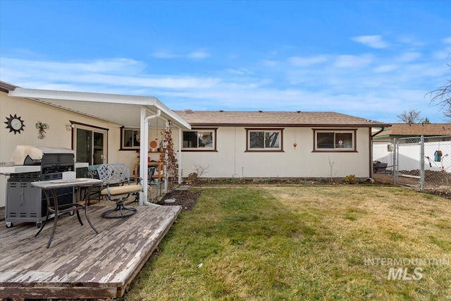 back of property with a deck, a lawn, and fence