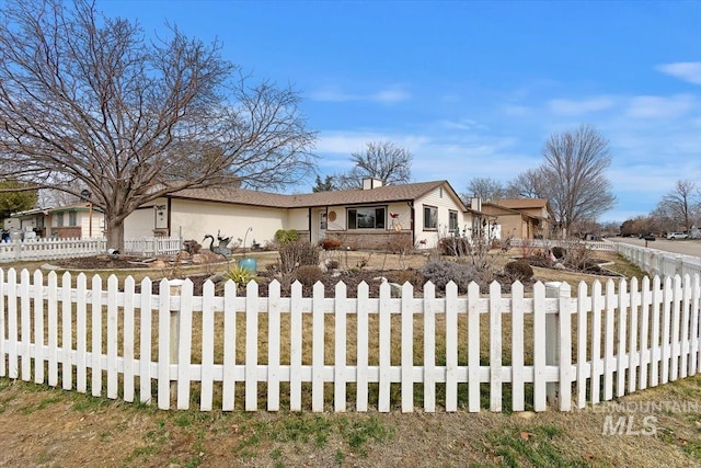 view of front of property with a fenced front yard, concrete driveway, a chimney, and stucco siding