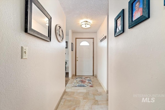 doorway to outside featuring baseboards, a textured ceiling, and a textured wall