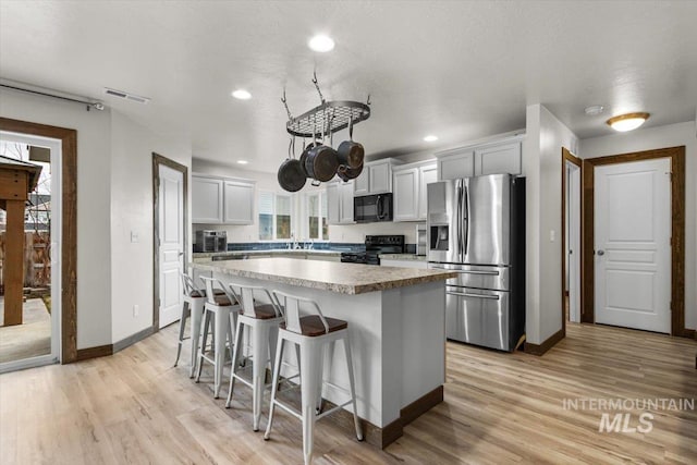 kitchen featuring a kitchen bar, black appliances, white cabinetry, light hardwood / wood-style floors, and a kitchen island