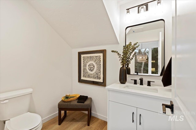 half bath featuring baseboards, toilet, wood finished floors, vaulted ceiling, and vanity