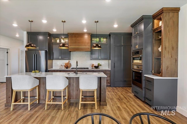 3160 Crescent Moon Rd, Twin Falls, ID 83301 - kitchen featuring stainless steel appliances, decorative backsplash, light wood-style floors, an island with sink, and decorative light fixtures