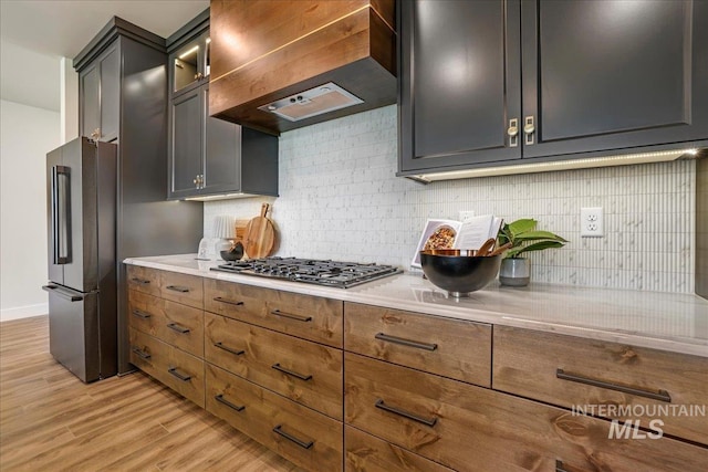 3160 Crescent Moon Rd, Twin Falls, ID 83301 - kitchen featuring appliances with stainless steel finishes, premium range hood, light countertops, light wood-style floors, and decorative backsplash