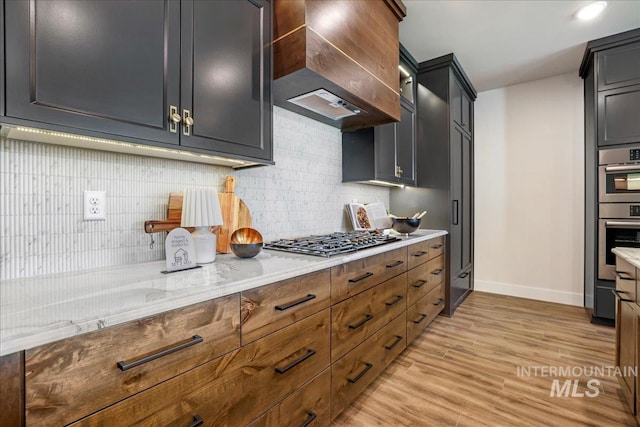 3160 Crescent Moon Rd, Twin Falls, ID 83301 - kitchen featuring stainless steel appliances, custom exhaust hood, light wood-type flooring, tasteful backsplash, and light stone countertops