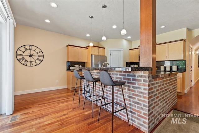 187 E Wishbone Ct, Boise, ID 83706 - kitchen featuring stainless steel refrigerator with ice dispenser, light brown cabinetry, dark countertops, baseboards, and a kitchen breakfast bar